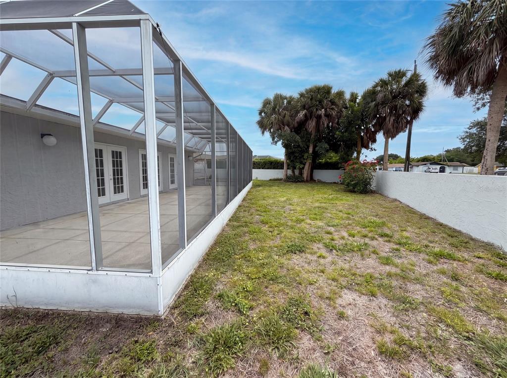 A screened-in patio overlooks a grassy backyard enclosed by a white wall and palm trees — 1301 LUCAYA AVENUE, VENICE, FL