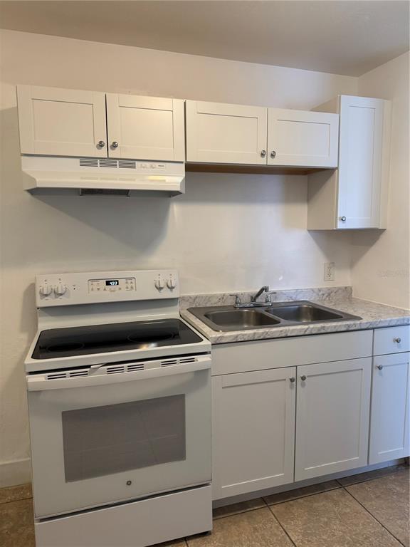 A kitchen features white cabinets, a white electric stove, and a double-basin sink with countertops — 930 EMERALD DRIVE, MOUNT DORA, FL