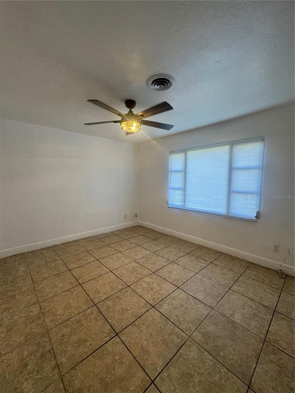 An empty room with beige tile flooring, white walls, a ceiling fan, and a window — 930 EMERALD DRIVE, MOUNT DORA, FL