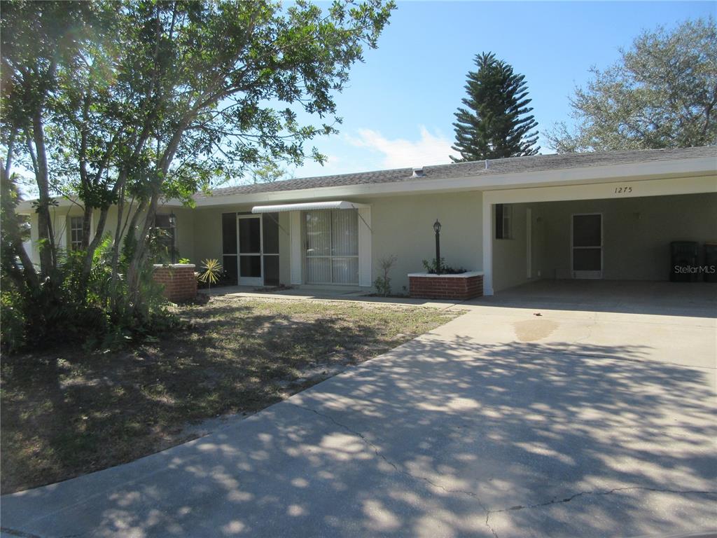 A single-story house features a light-colored exterior, a concrete driveway, and an attached carport — 1275 PRICE CIRCLE NW, PORT CHARLOTTE, FL