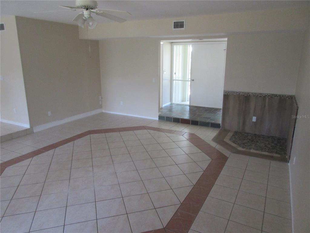 An interior room features light-colored tile flooring with a decorative border and a stone fireplace — 1275 PRICE CIRCLE NW, PORT CHARLOTTE, FL