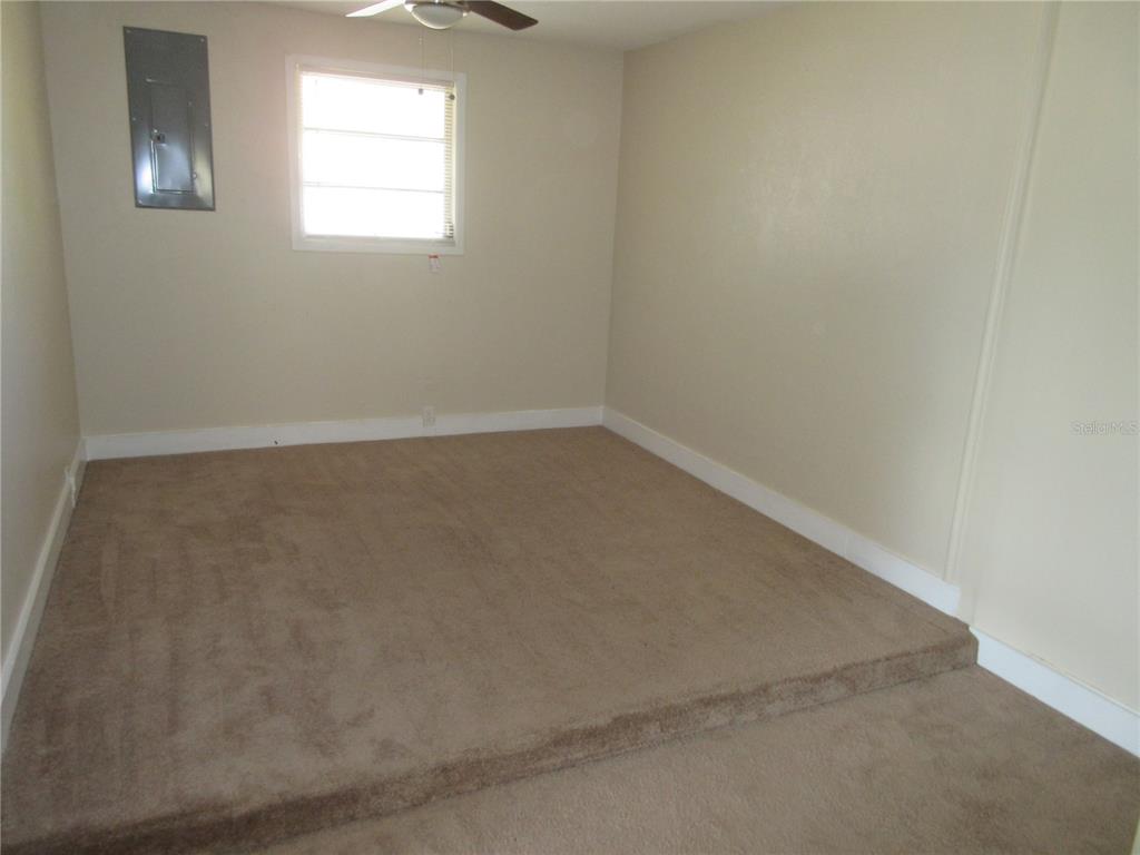 A carpeted room features a raised platform area, a ceiling fan, and a wall-mounted electrical panel — 1275 PRICE CIRCLE NW, PORT CHARLOTTE, FL