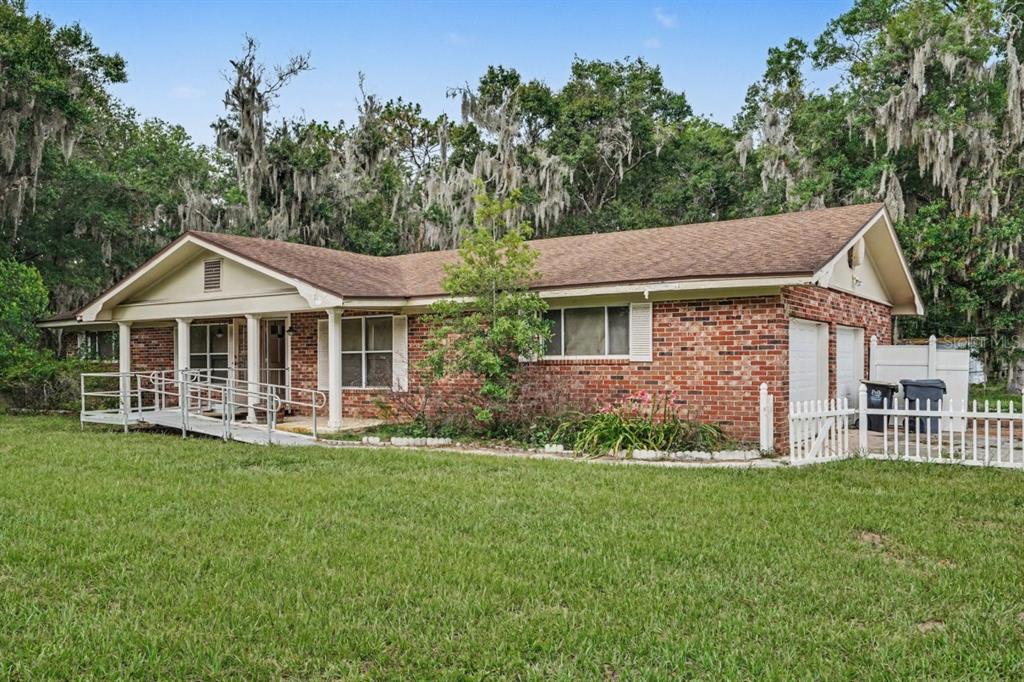 A single-story brick house with a metal wheelchair ramp and a white picket fence — 4921 DEESON ROAD, LAKELAND, FL