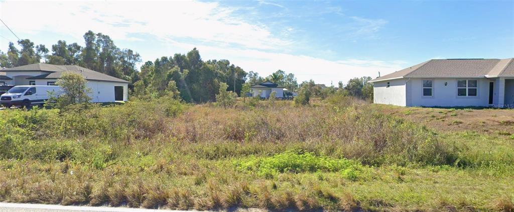 A vacant, grassy lot sits between two modern single-family homes under a blue sky — 3217 40TH STREET SW, LEHIGH ACRES, FL