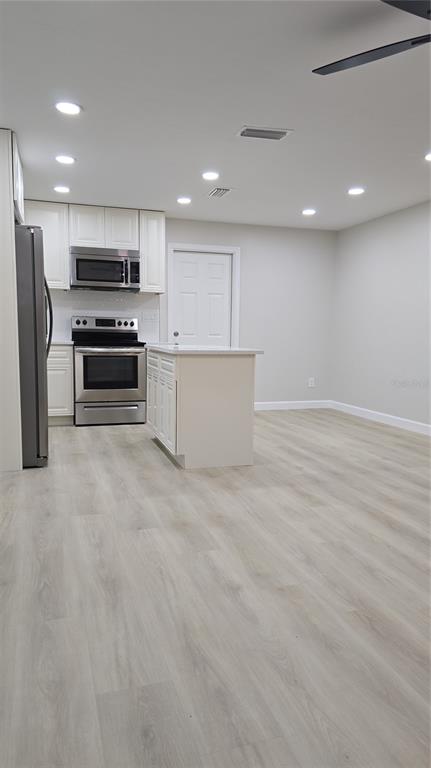 A kitchen features white cabinets, stainless steel appliances, a small island, and light wood flooring — 1504 SE 12TH PLACE, GAINESVILLE, FL