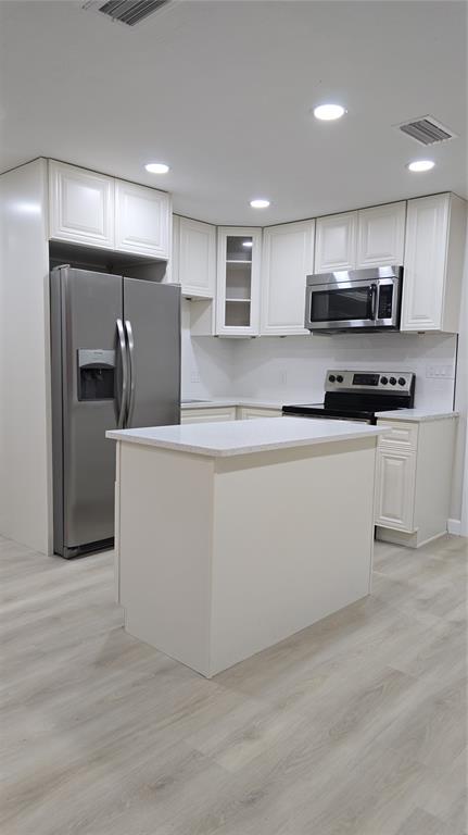 A kitchen features white cabinetry, stainless steel appliances, a center island, and light wood flooring — 1504 SE 12TH PLACE, GAINESVILLE, FL