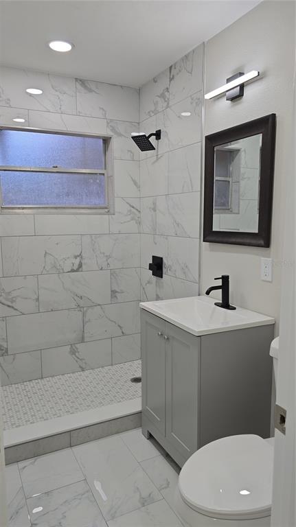 A bathroom features a walk-in shower with marble-look tile, a gray vanity, and black fixtures — 1504 SE 12TH PLACE, GAINESVILLE, FL