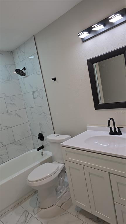 A bathroom features a white vanity, a toilet, and a tub with marble-look tile walls — 1504 SE 12TH PLACE, GAINESVILLE, FL