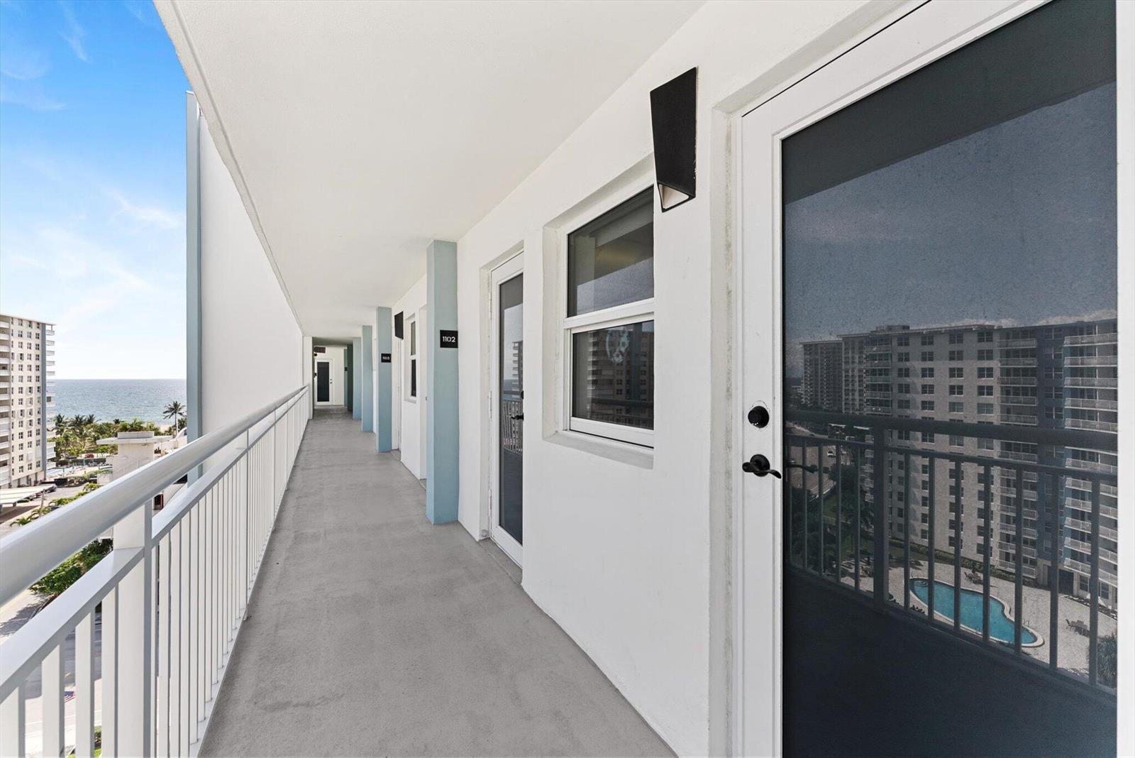 An outdoor walkway with white railings overlooks the ocean and a neighboring building — 201 N Ocean Boulevard # 1102, Pompano Beach FL 33062, POMPANO BEACH, FL
