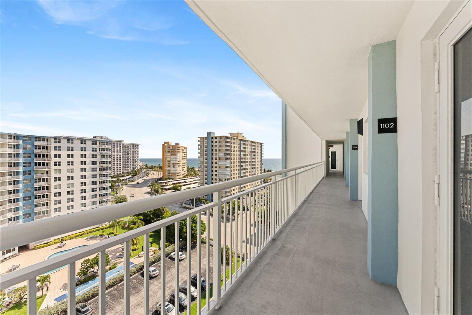 An outdoor apartment building walkway overlooks a parking lot, swimming pool, and the ocean — 201 N Ocean Boulevard # 1102, Pompano Beach FL 33062, POMPANO BEACH, FL