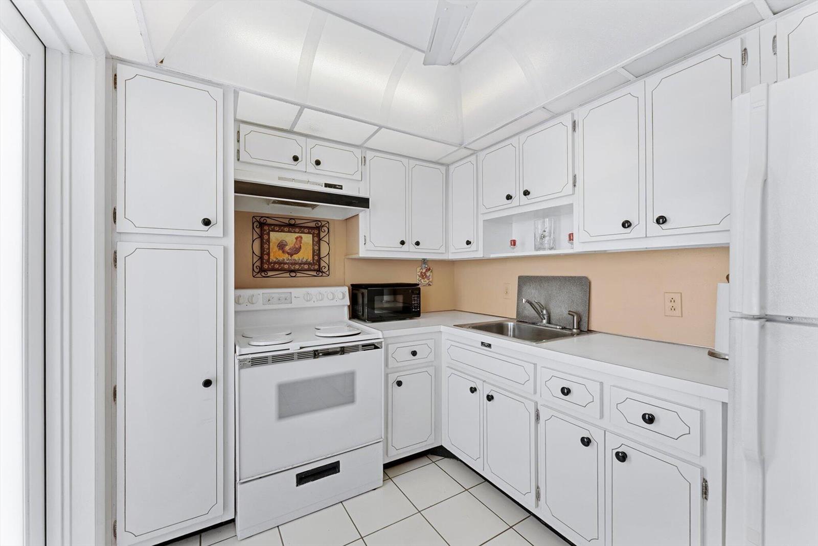 A white kitchen features white cabinets, a white stove, and a stainless steel sink — 201 N Ocean Boulevard # 1102, Pompano Beach FL 33062, POMPANO BEACH, FL