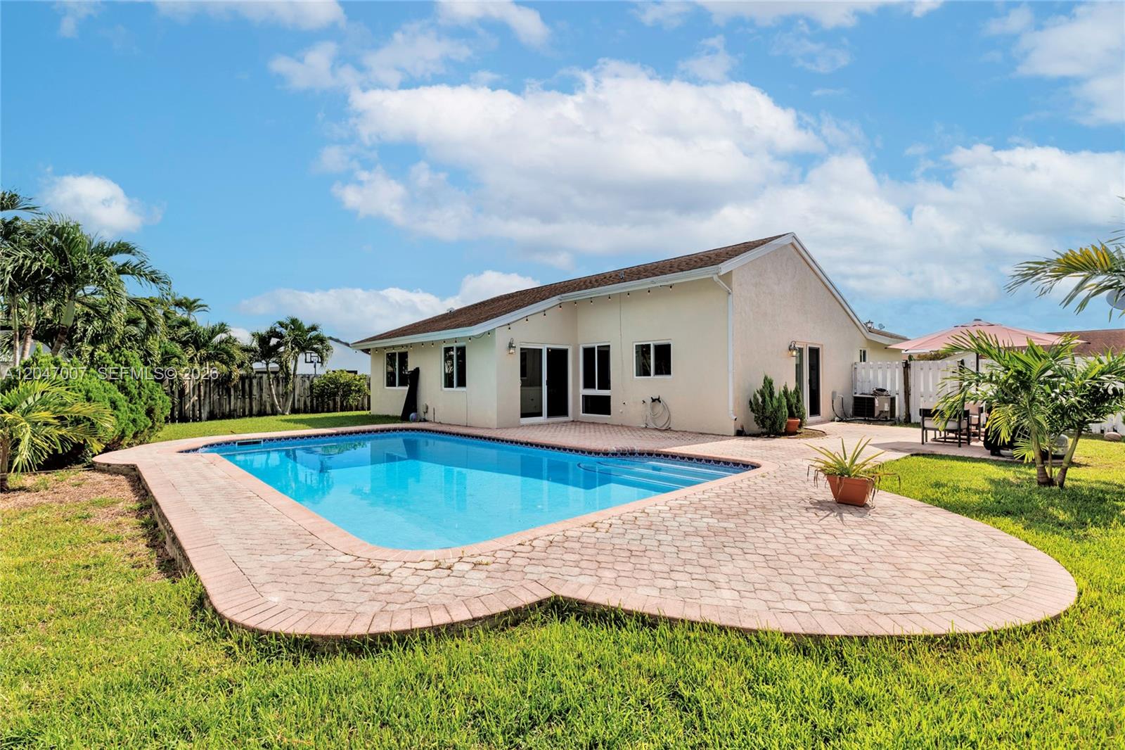 A backyard features a rectangular swimming pool with a brick paver deck and green lawn — 681 Pine Ridge Ter, Davie FL 33325, DAVIE, FL