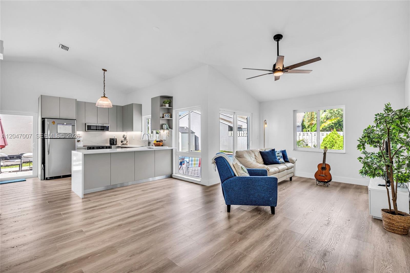 A modern open-concept living area features a gray kitchen, light wood flooring, and a ceiling fan — 681 Pine Ridge Ter, Davie FL 33325, DAVIE, FL