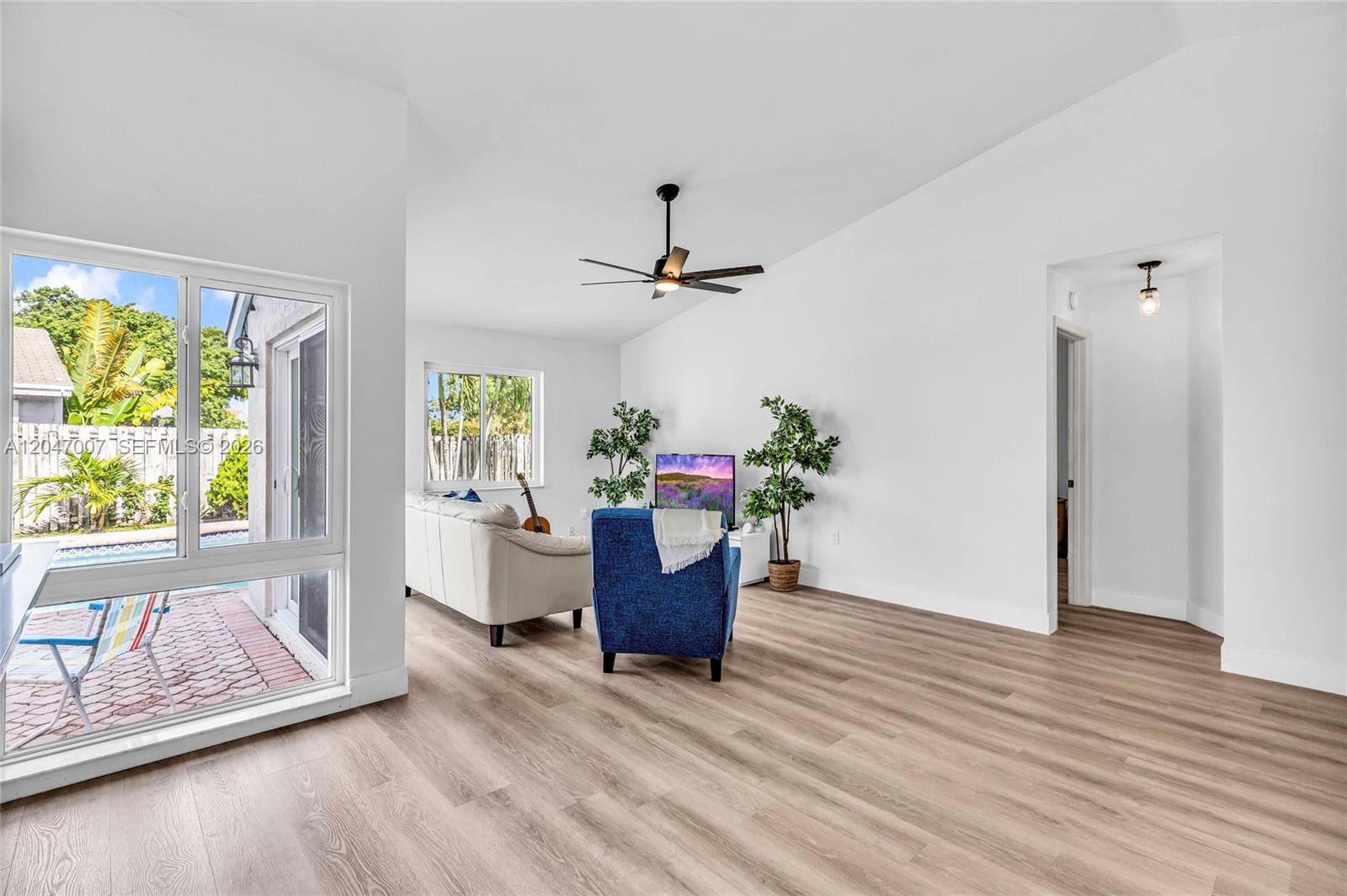 A living room features light wood-look flooring, white walls, a ceiling fan, and a sliding glass door — 681 Pine Ridge Ter, Davie FL 33325, DAVIE, FL