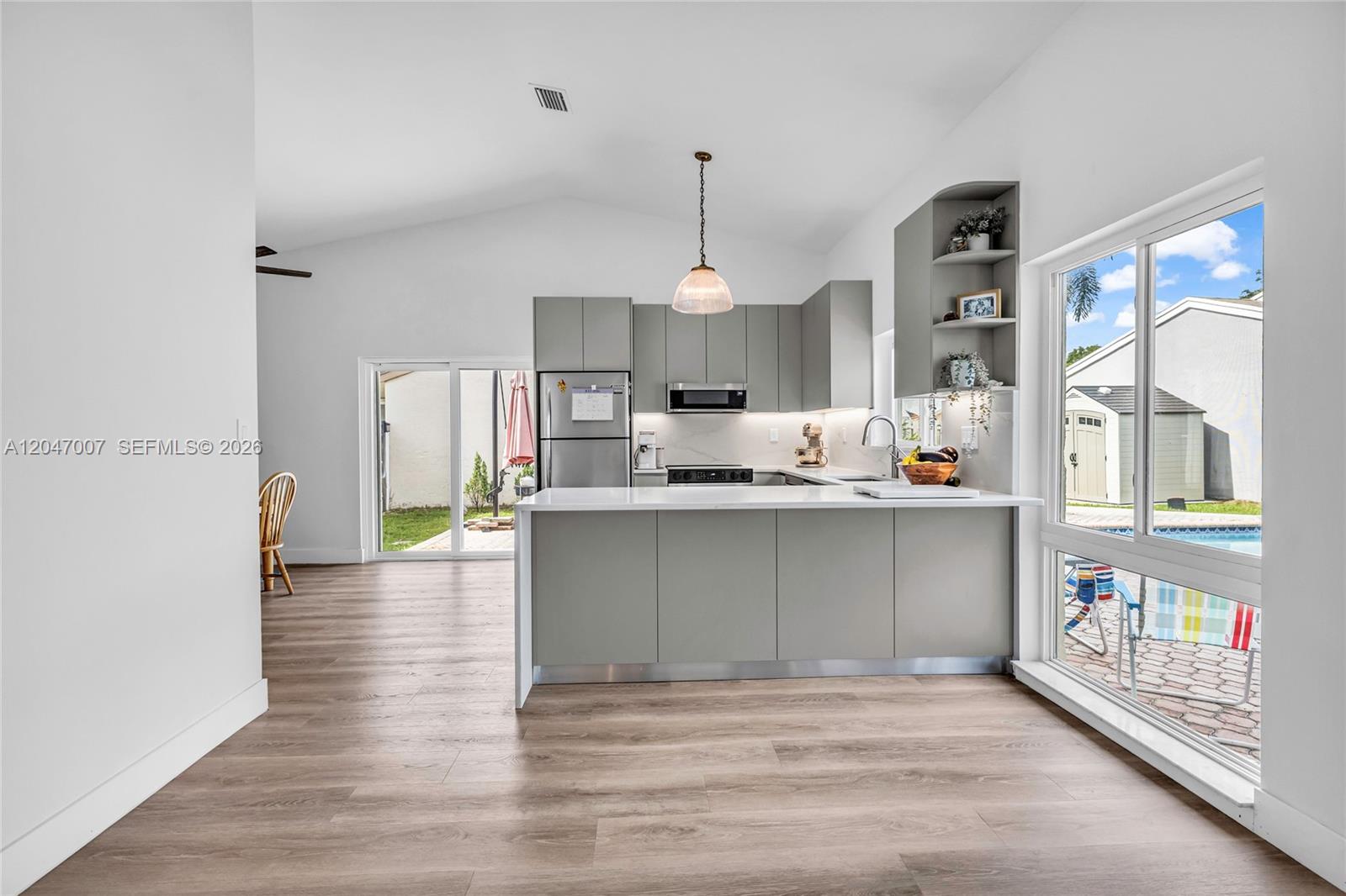 A modern kitchen features gray flat-panel cabinets, a white quartz island, and wood-look flooring — 681 Pine Ridge Ter, Davie FL 33325, DAVIE, FL