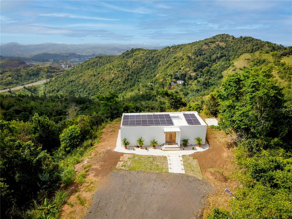 An aerial view shows a house with solar panels situated on a forested hillside lot — Bo Sumido 7737 KM 1 6, CAYEY, PR