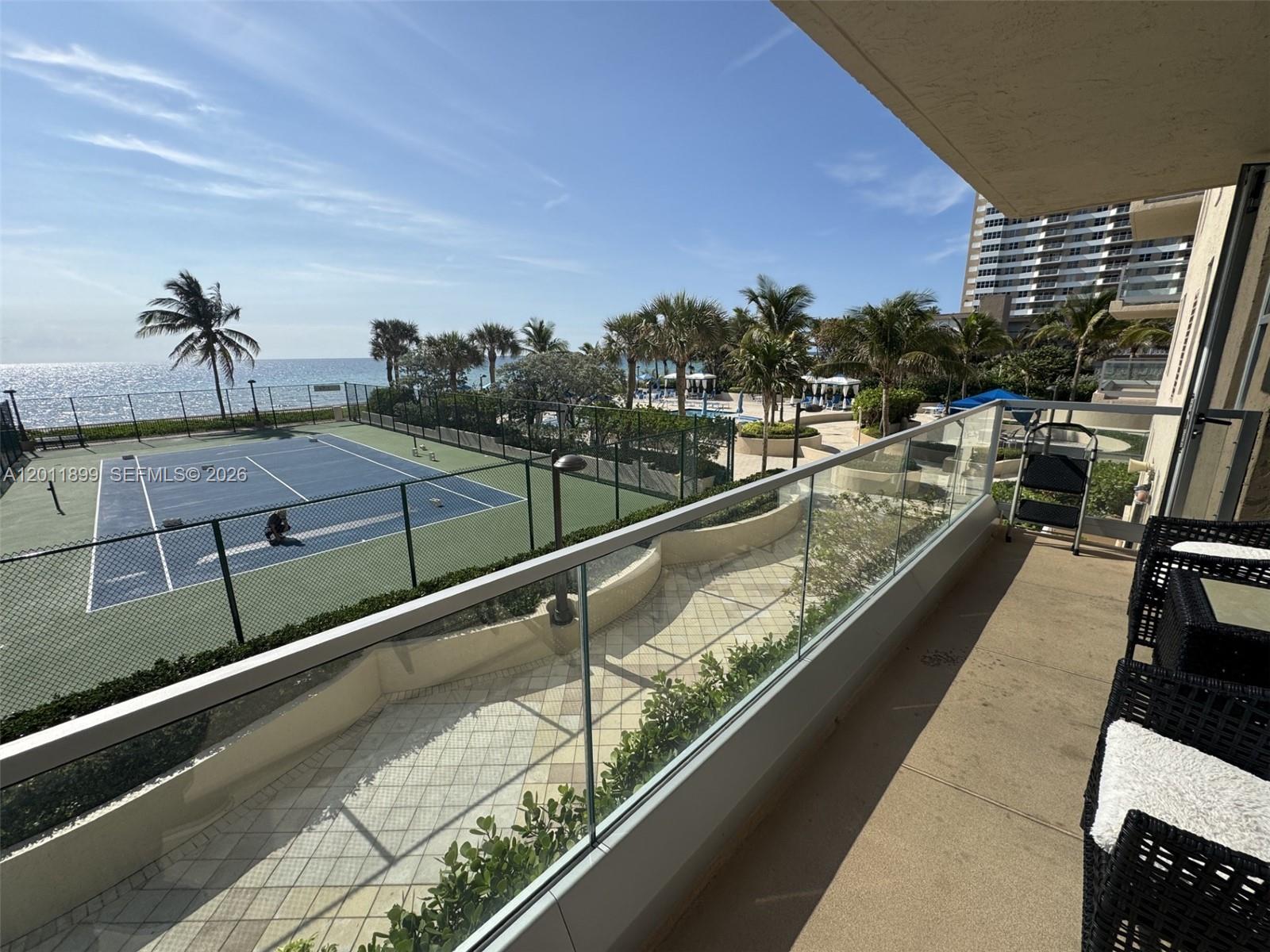 A balcony overlooks a tennis court, swimming pool area, and the ocean — 1912 S Ocean Dr # 3D, Hallandale Beach FL 33009, HALLANDALE BEACH, FL