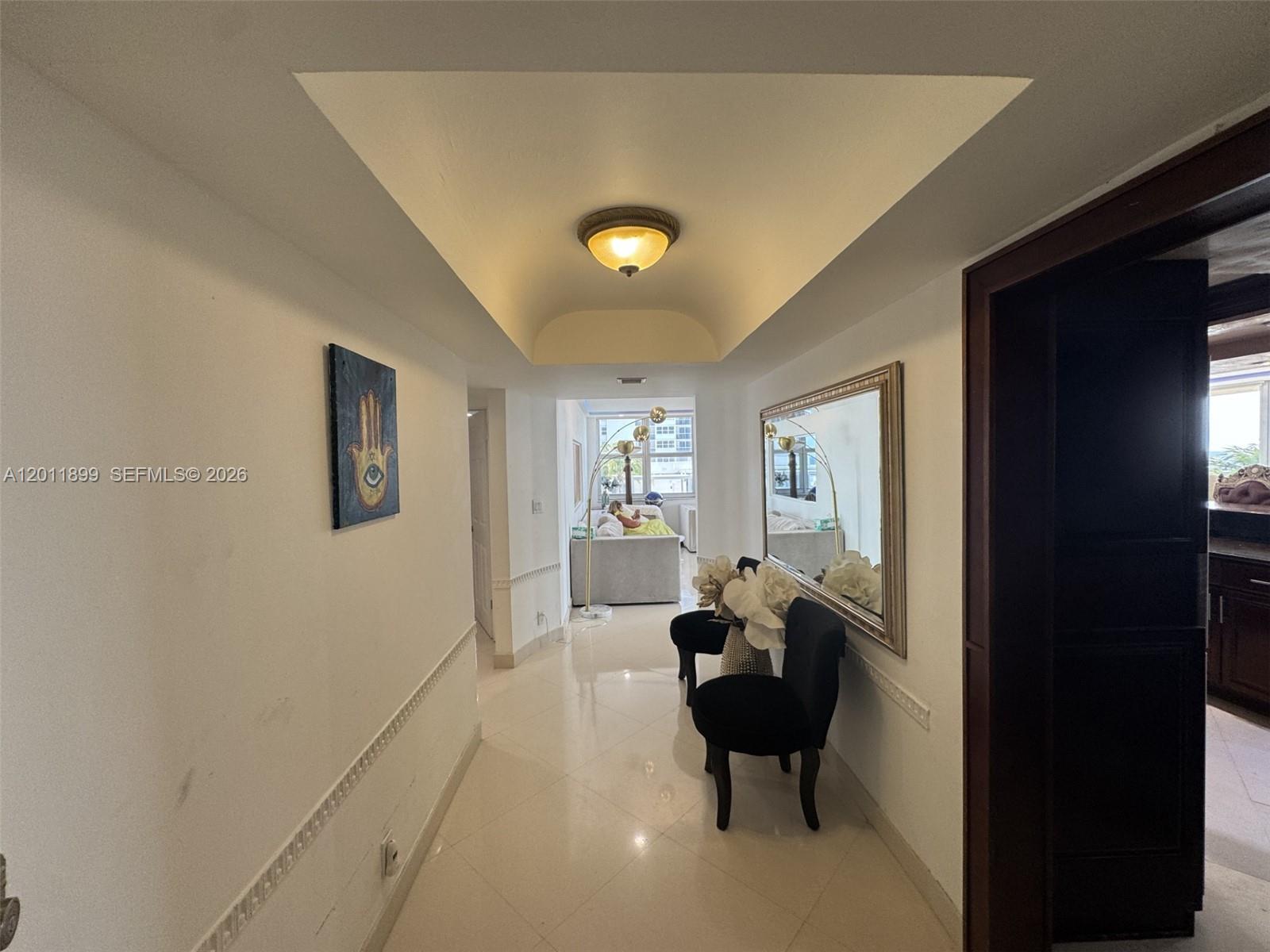 A hallway with white walls, tile flooring, a tray ceiling, and two black chairs — 1912 S Ocean Dr # 3D, Hallandale Beach FL 33009, HALLANDALE BEACH, FL