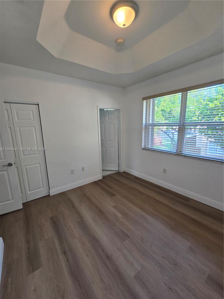 An empty bedroom features wood-look flooring, a tray ceiling, and a window with blinds — 1575 NE 33rd Ave # 9, Homestead FL 33033, HOMESTEAD, FL