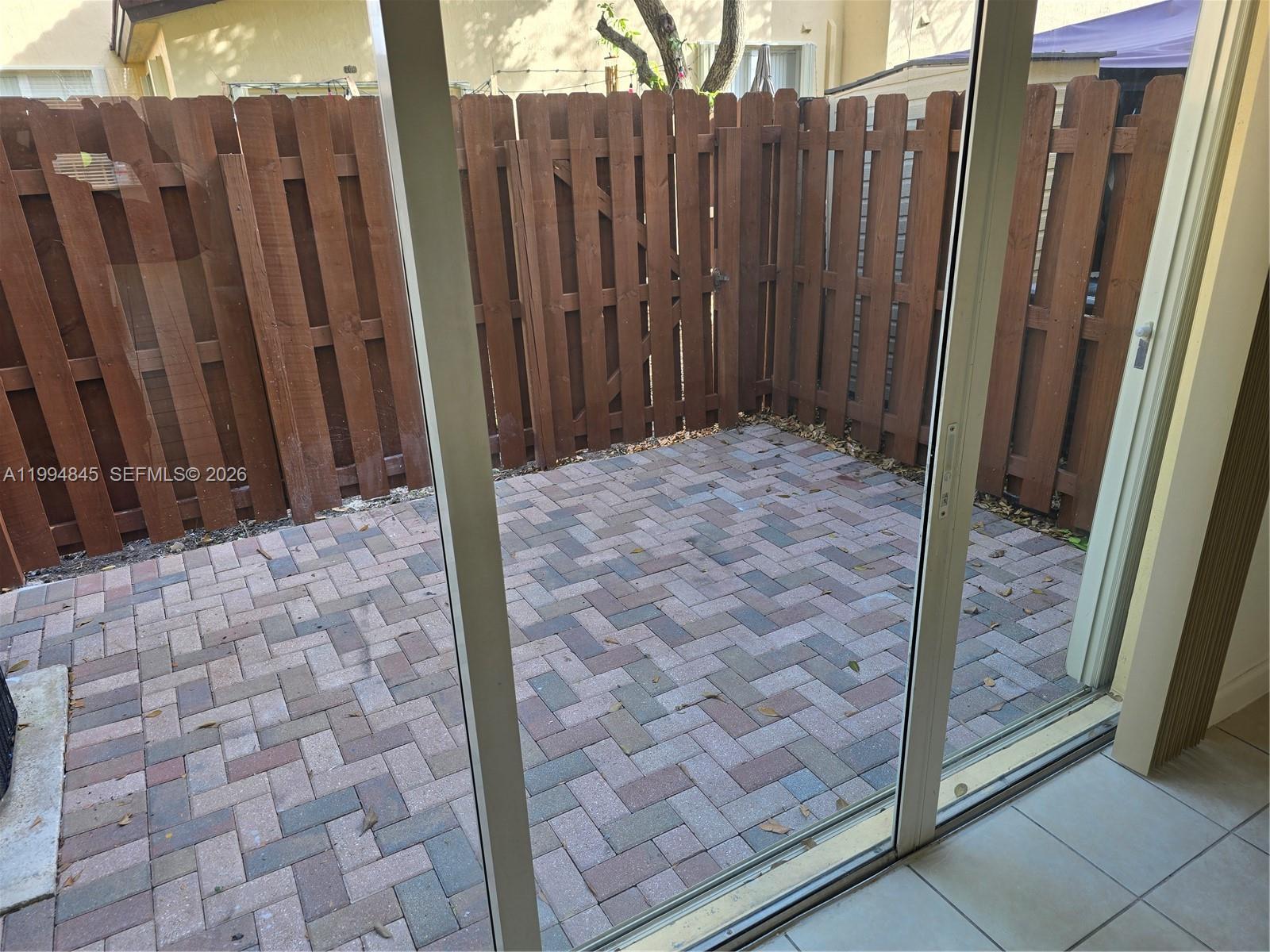 A paved patio is enclosed by a wooden fence and viewed through a sliding glass door — 1575 NE 33rd Ave # 9, Homestead FL 33033, HOMESTEAD, FL