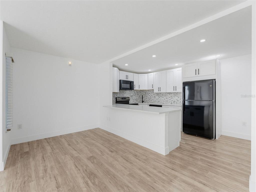 A kitchen with white cabinets, a black refrigerator, and a breakfast bar overlooks a room — 1261 PINE RIDGE CIRCLE W UNIT D1, TARPON SPRINGS, FL