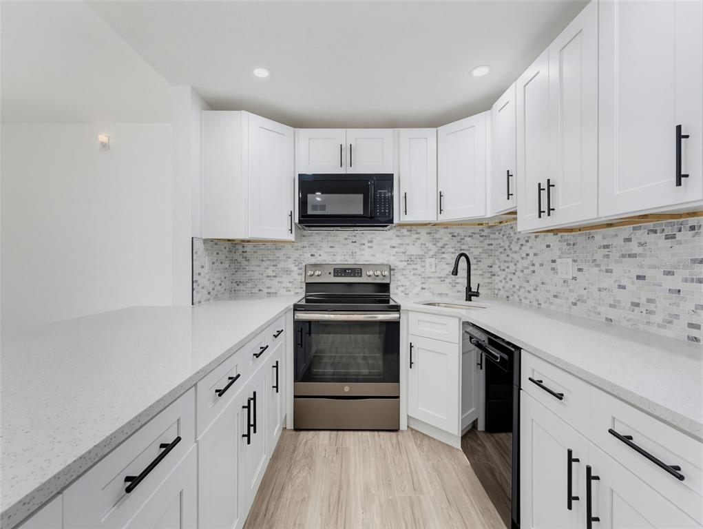 A kitchen features white cabinets, quartz countertops, a mosaic tile backsplash, and stainless steel appliances — 1261 PINE RIDGE CIRCLE W UNIT D1, TARPON SPRINGS, FL