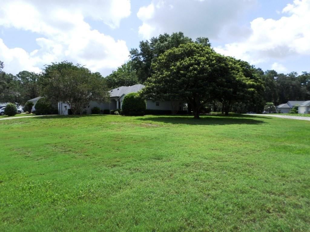 A large, grassy front yard leads to a single-story house shaded by mature trees — 9093 SW 192ND COURT RD, DUNNELLON, FL