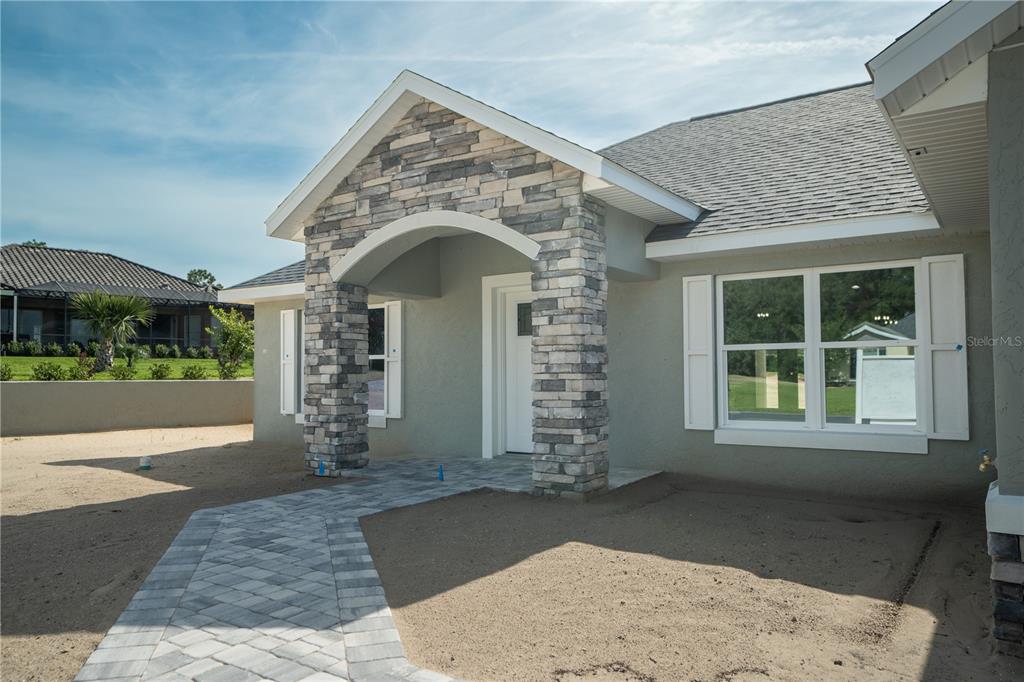 The exterior of a house features a stone-accented entryway, a paved walkway, and gray stucco — 6595 SW 179TH COURT ROAD, DUNNELLON, FL