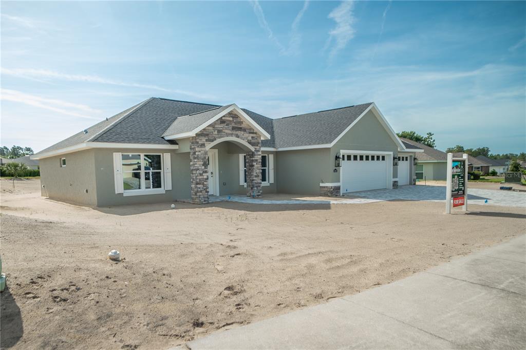 A single-story house with a stone-accented entryway, white garage doors, and an unfinished sandy yard — 6595 SW 179TH COURT ROAD, DUNNELLON, FL