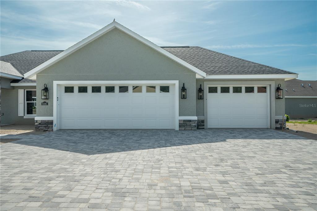 A house exterior features a three-car garage with white doors and a paved driveway — 6595 SW 179TH COURT ROAD, DUNNELLON, FL
