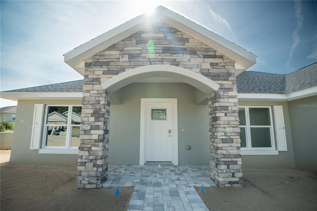The exterior of a house features a stone-accented entryway, a white front door, and windows — 6595 SW 179TH COURT ROAD, DUNNELLON, FL