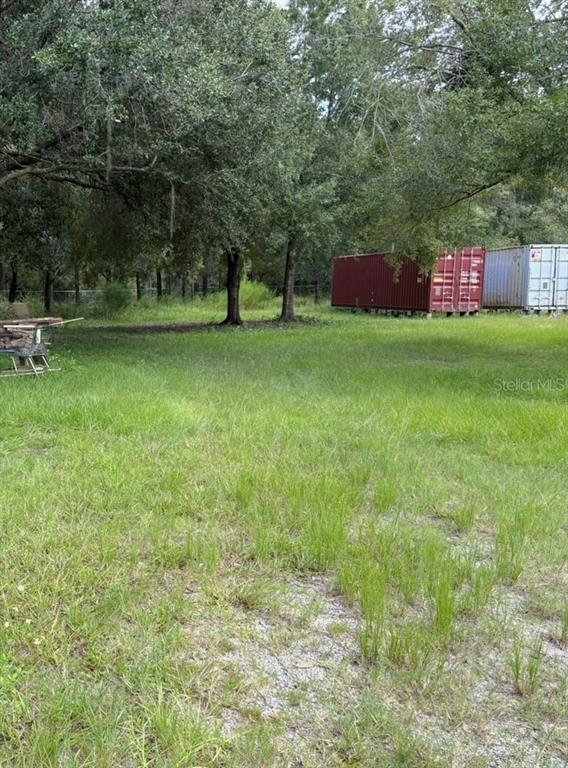 A grassy lot features several large shipping containers positioned near a line of trees — 5585 LAKE LIZZIE DRIVE, ST CLOUD, FL