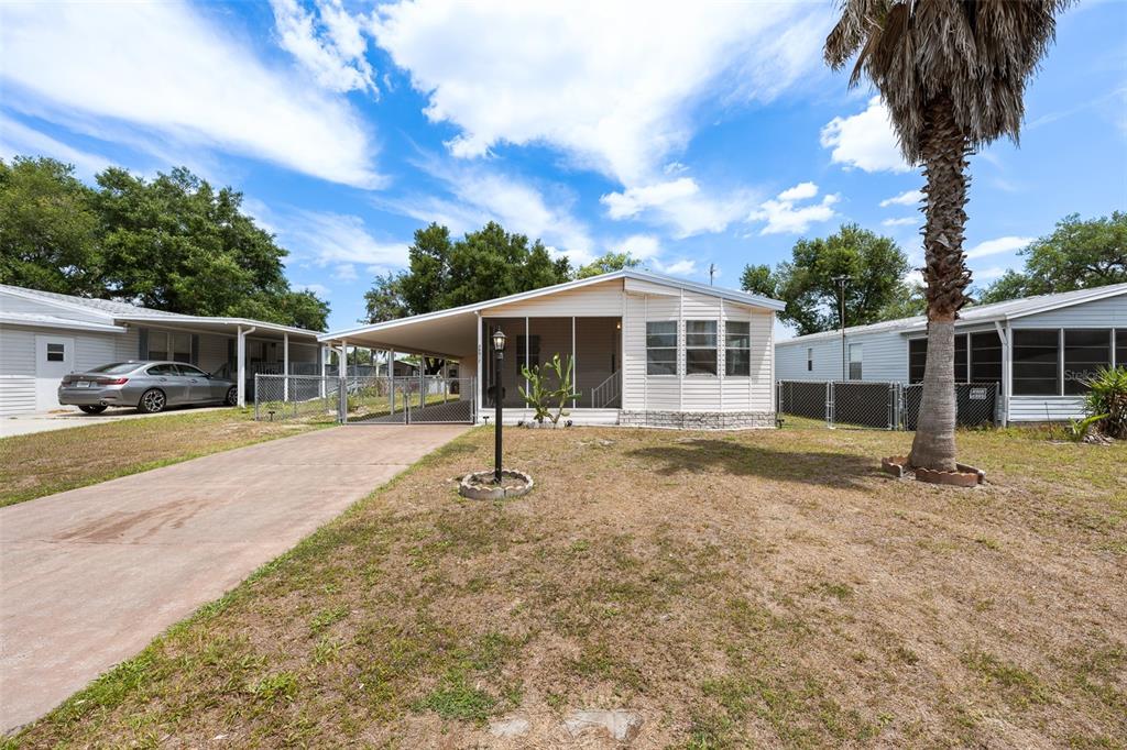 A single-story manufactured home features a screened-in porch, a carport, and a palm tree — 38052 LAWANDA LOOP, ZEPHYRHILLS, FL