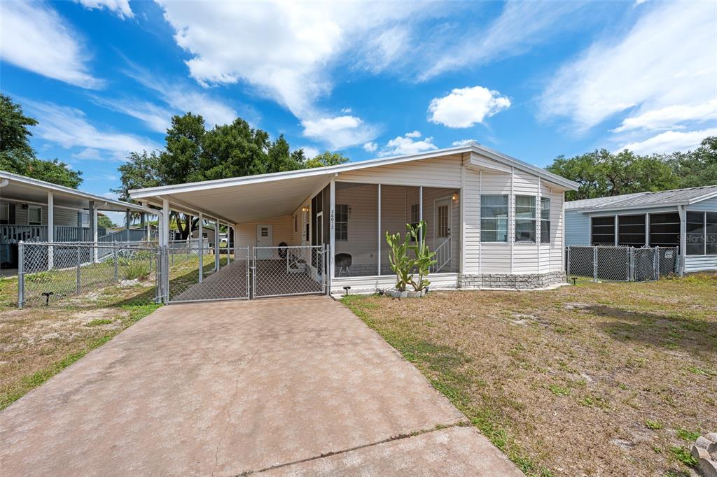 A single-story manufactured home with a carport, screened-in porch, and chain-link fencing — 38052 LAWANDA LOOP, ZEPHYRHILLS, FL