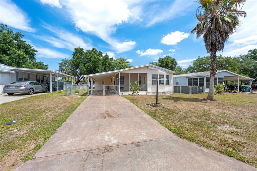 A single-story manufactured home with a concrete driveway, carport, and screened porch under a sky — 38052 LAWANDA LOOP, ZEPHYRHILLS, FL