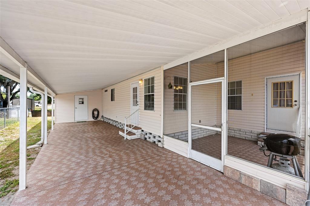 A covered concrete carport sits beside a home with a screened-in porch and beige siding — 38052 LAWANDA LOOP, ZEPHYRHILLS, FL