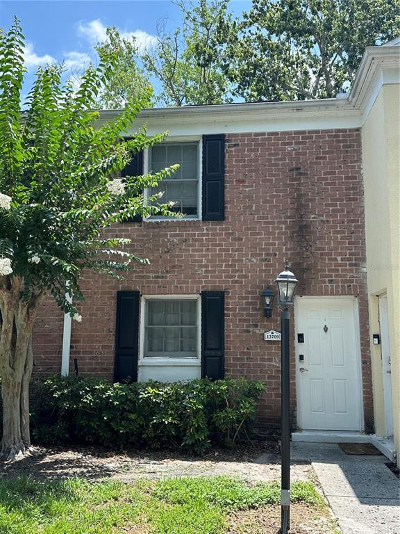 A two-story brick townhouse exterior features black shutters, a white front door, and a lamppost — 13709 JUNIPER BLOSSOM DRIVE UNIT 0, TAMPA, FL