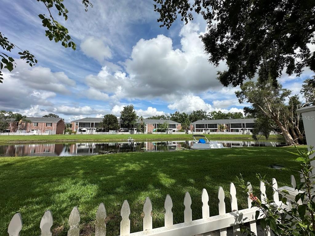 A grassy lawn leads to a lake with a bench and trees under a blue sky — 13709 JUNIPER BLOSSOM DRIVE UNIT 0, TAMPA, FL