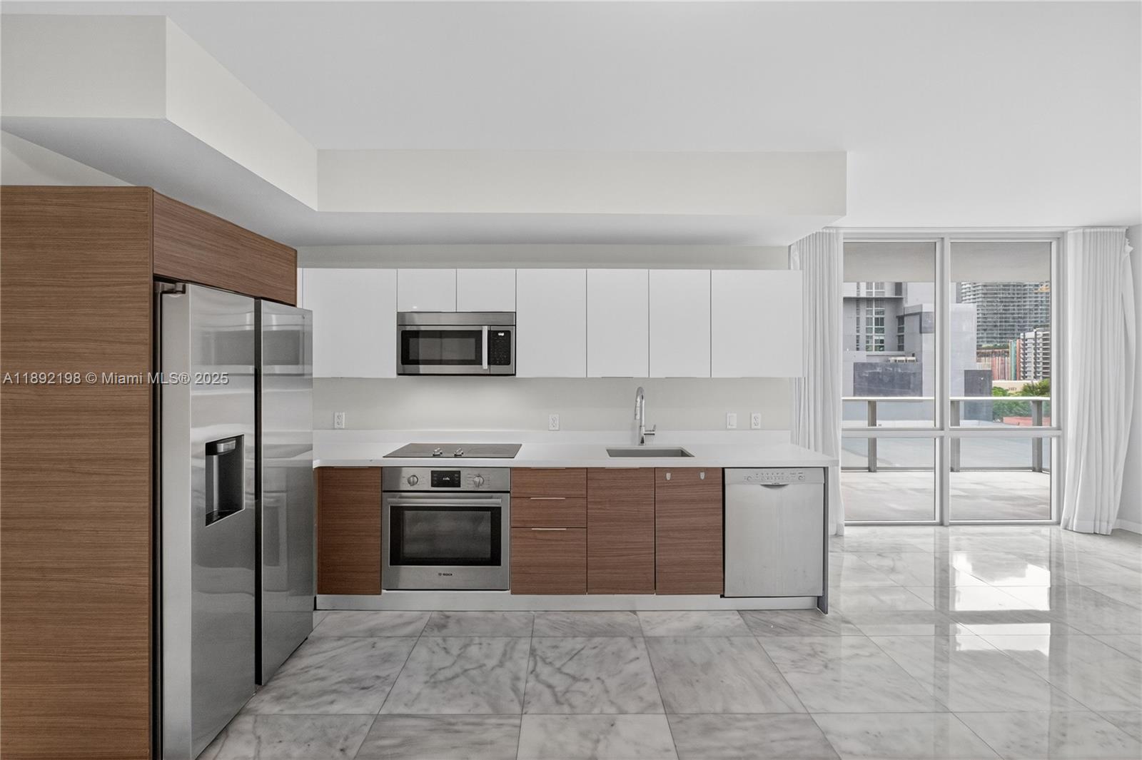 A modern kitchen features white upper cabinets, wood-toned lower cabinets, stainless steel appliances, and marble flooring — 1010 SW 2nd Ave # 603, Miami FL 33130, MIAMI, FL
