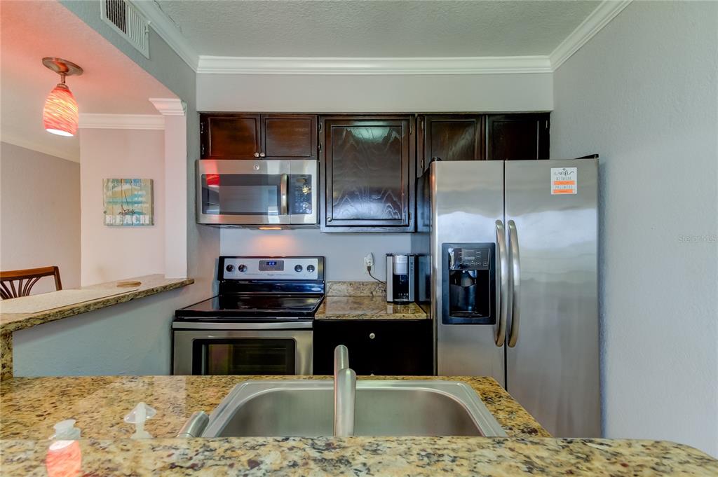 A kitchen features dark wood cabinets, stainless steel appliances, and granite countertops — 2506 N ROCKY POINT DRIVE UNIT 457, TAMPA, FL