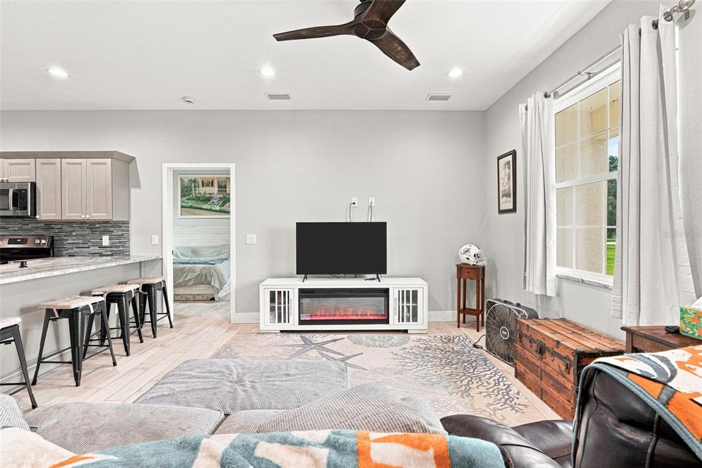 A living room features a TV stand with an electric fireplace, light flooring, and stools — 4651 SW PROVAU AVENUE, ARCADIA, FL