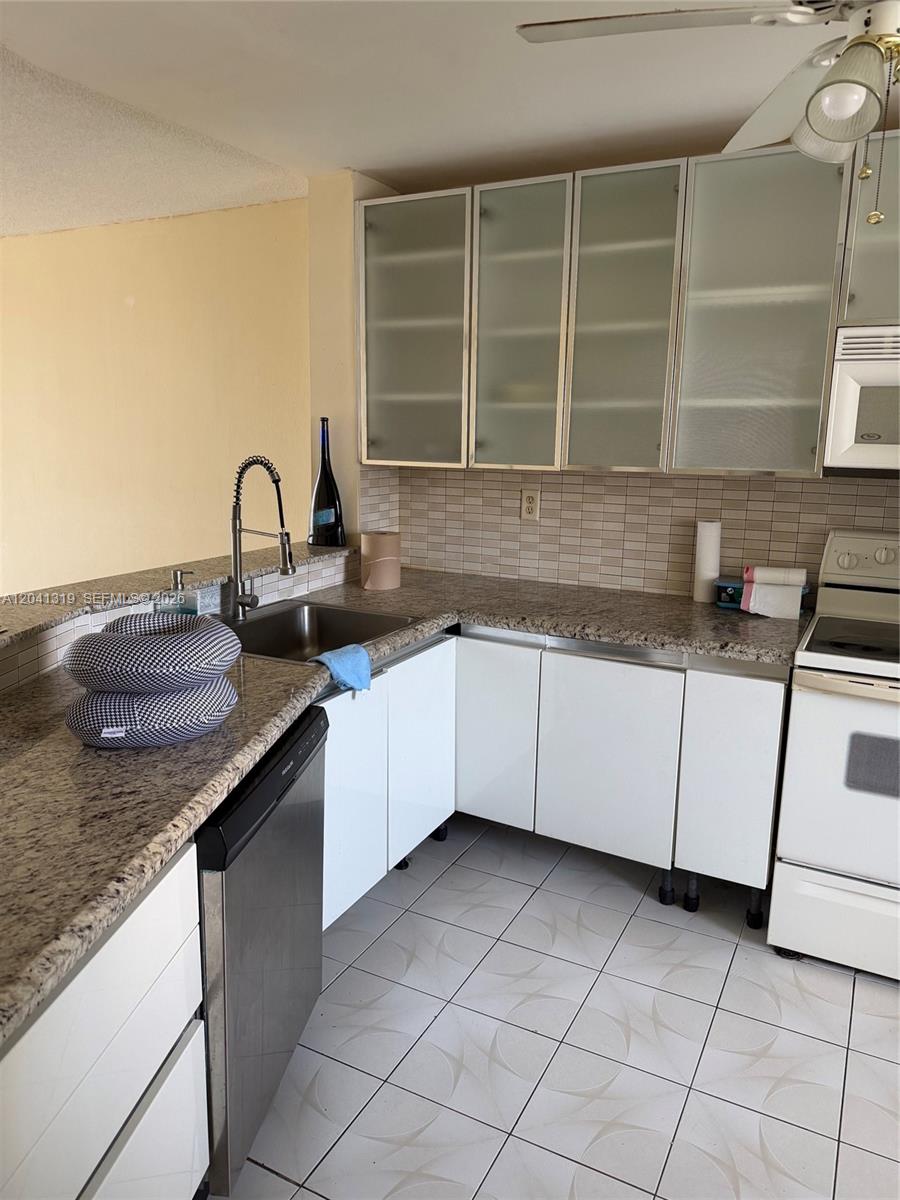 A kitchen features white cabinets, granite countertops, a stainless steel sink, and tiled flooring — 1750 NE 191st St # 4, Miami FL 33179, MIAMI, FL