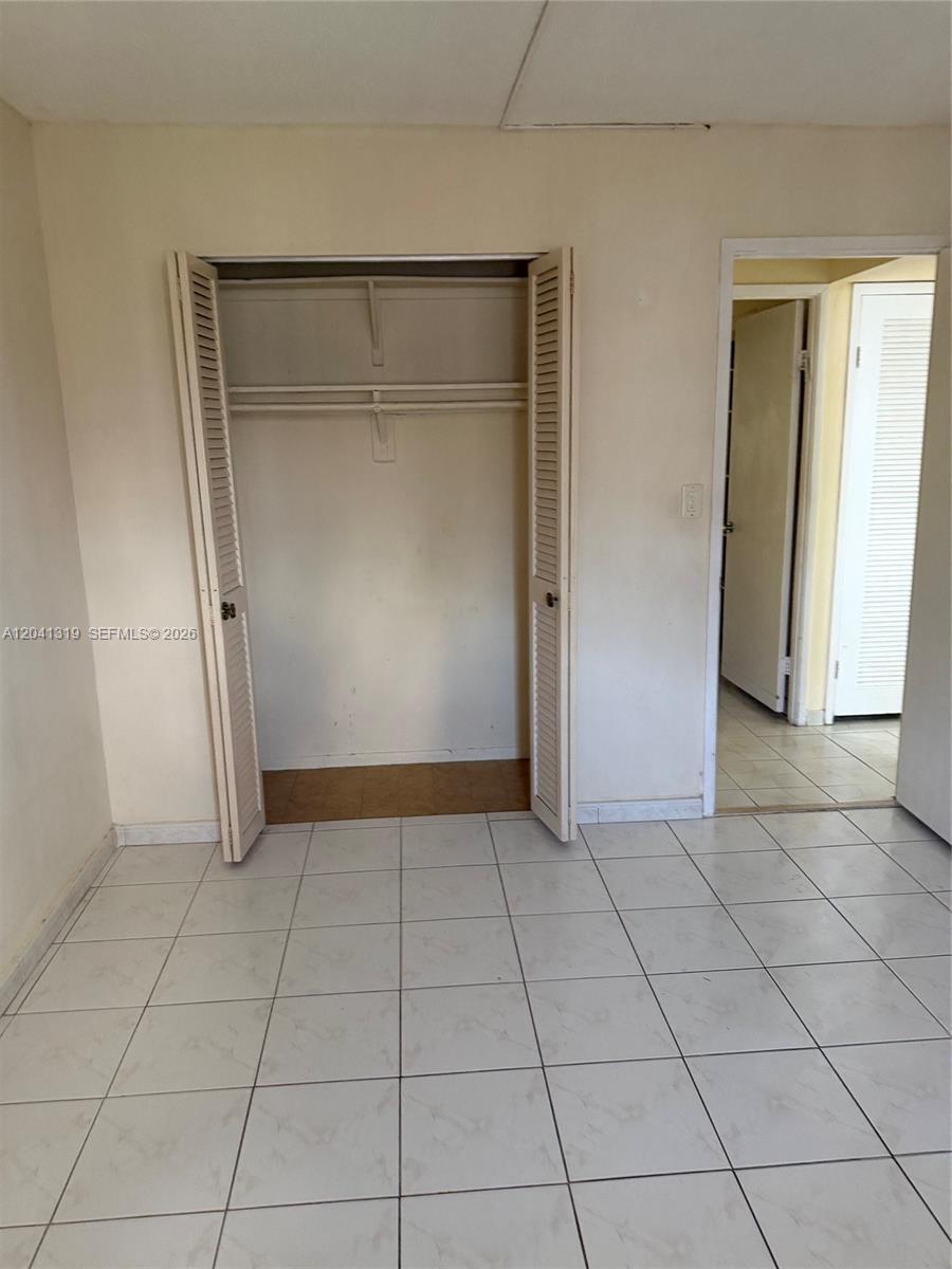 A room with white tiled floors, a closet with louvered doors, and an open doorway — 1750 NE 191st St # 4, Miami FL 33179, MIAMI, FL