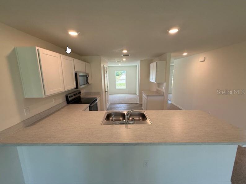 A kitchen with white cabinets, a laminate countertop, and a double sink overlooks an open area — 1 RIVERVIEW PLACE, PALM COAST, FL