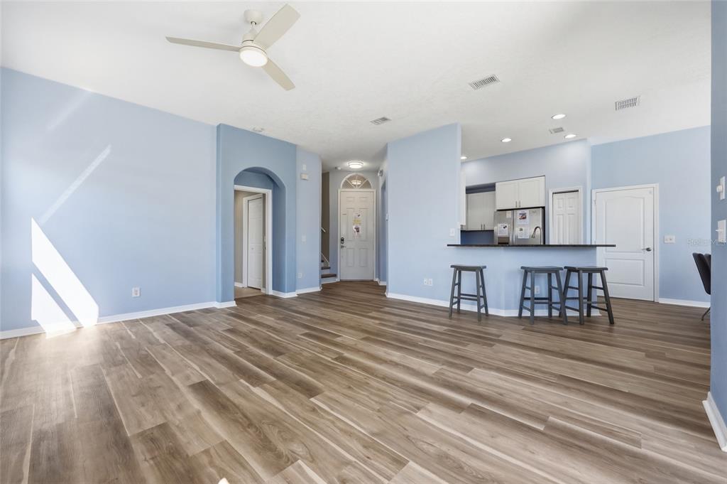 A living room with light blue walls, wood-look flooring, and an open kitchen with stools — 720 BRUNELLO DRIVE, DAVENPORT, FL
