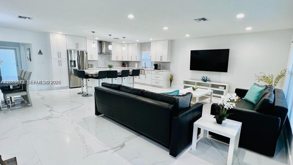A modern open-concept living room and kitchen feature white cabinetry, marble-look flooring, and black sofas — 218 SE 3rd Pl # 0, Dania Beach FL 33004, DANIA BEACH, FL