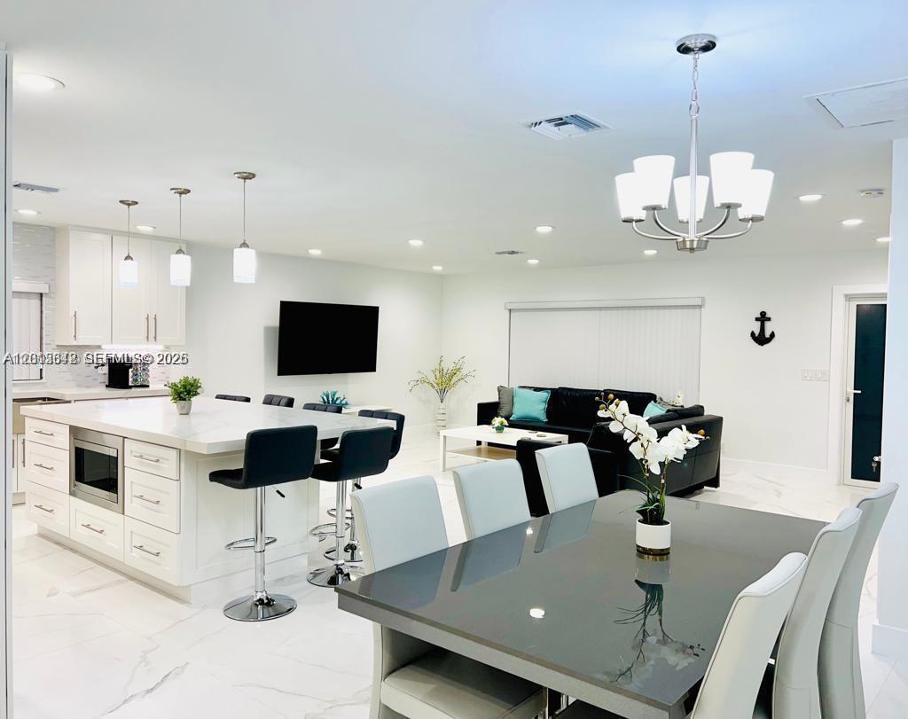 An open-concept kitchen, dining area, and living room featuring white cabinetry and marble-look flooring — 218 SE 3rd Pl # 0, Dania Beach FL 33004, DANIA BEACH, FL