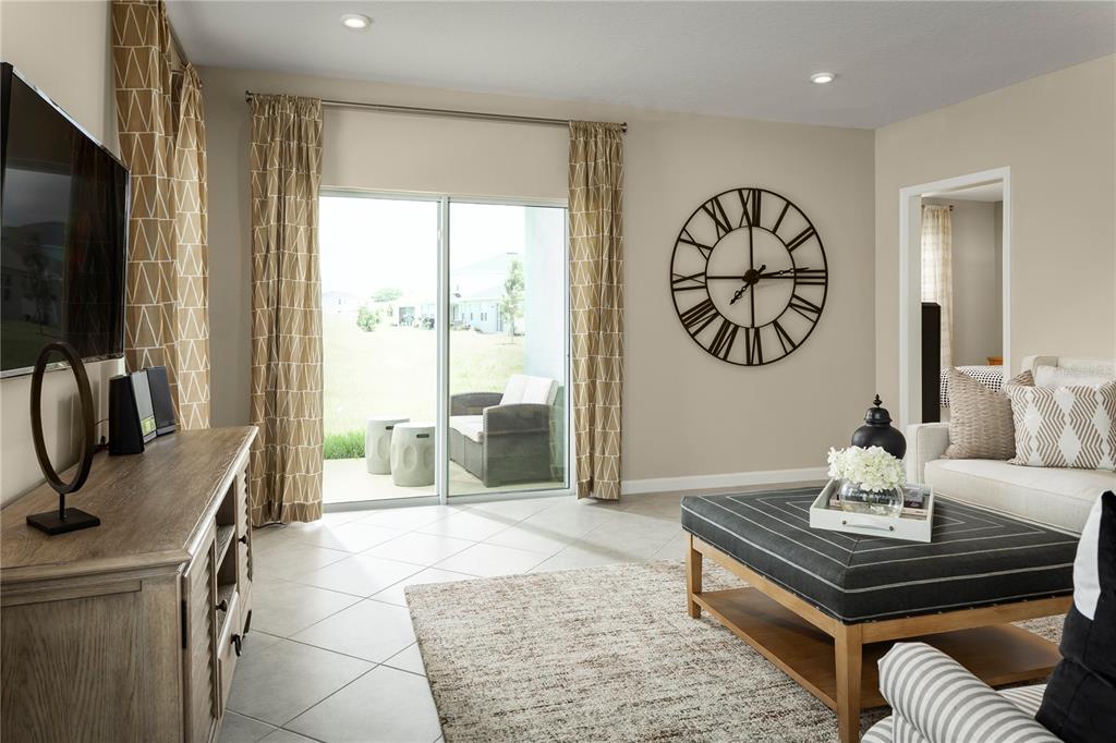 A living room features a large wall clock, sliding glass doors, and a central ottoman — 2445 WHITE LADYFISH ROAD, WIMAUMA, FL