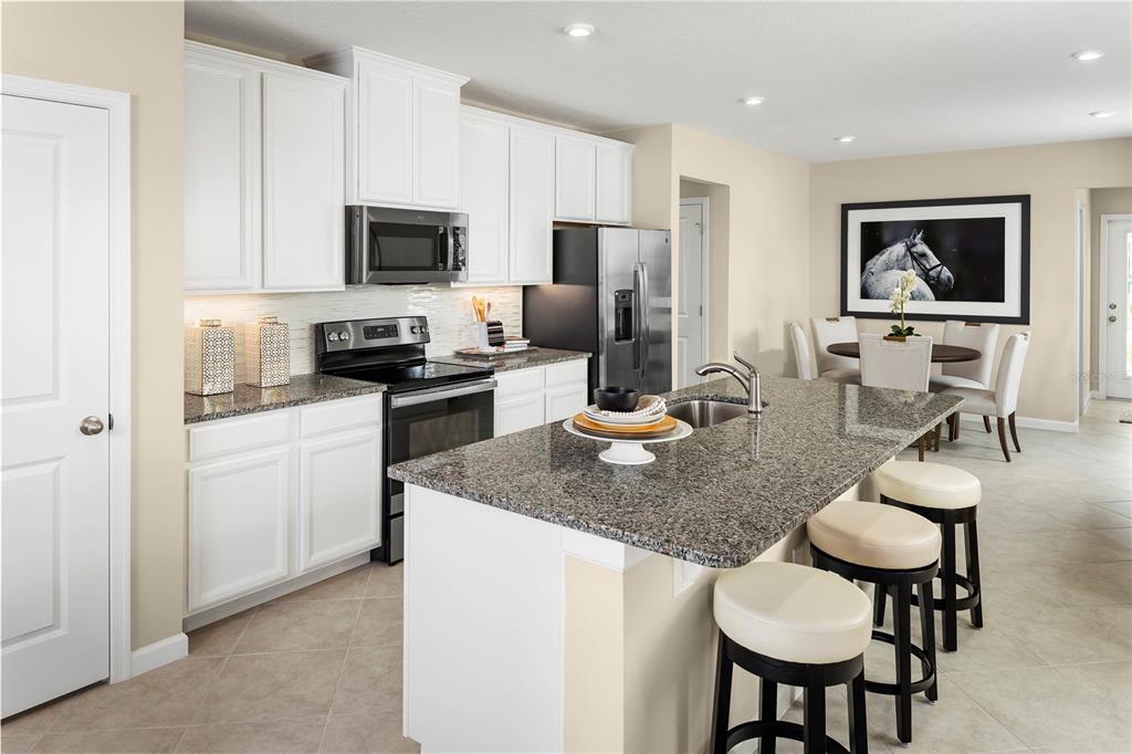 A kitchen with white cabinets, granite countertops, a center island, and an adjacent dining area — 2445 WHITE LADYFISH ROAD, WIMAUMA, FL