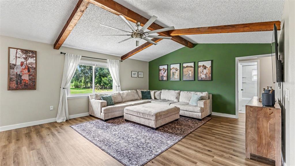 A living room features a vaulted ceiling with exposed beams, a green accent wall, and sectional — 5303 KNIGHTS STATION ROAD, LAKELAND, FL